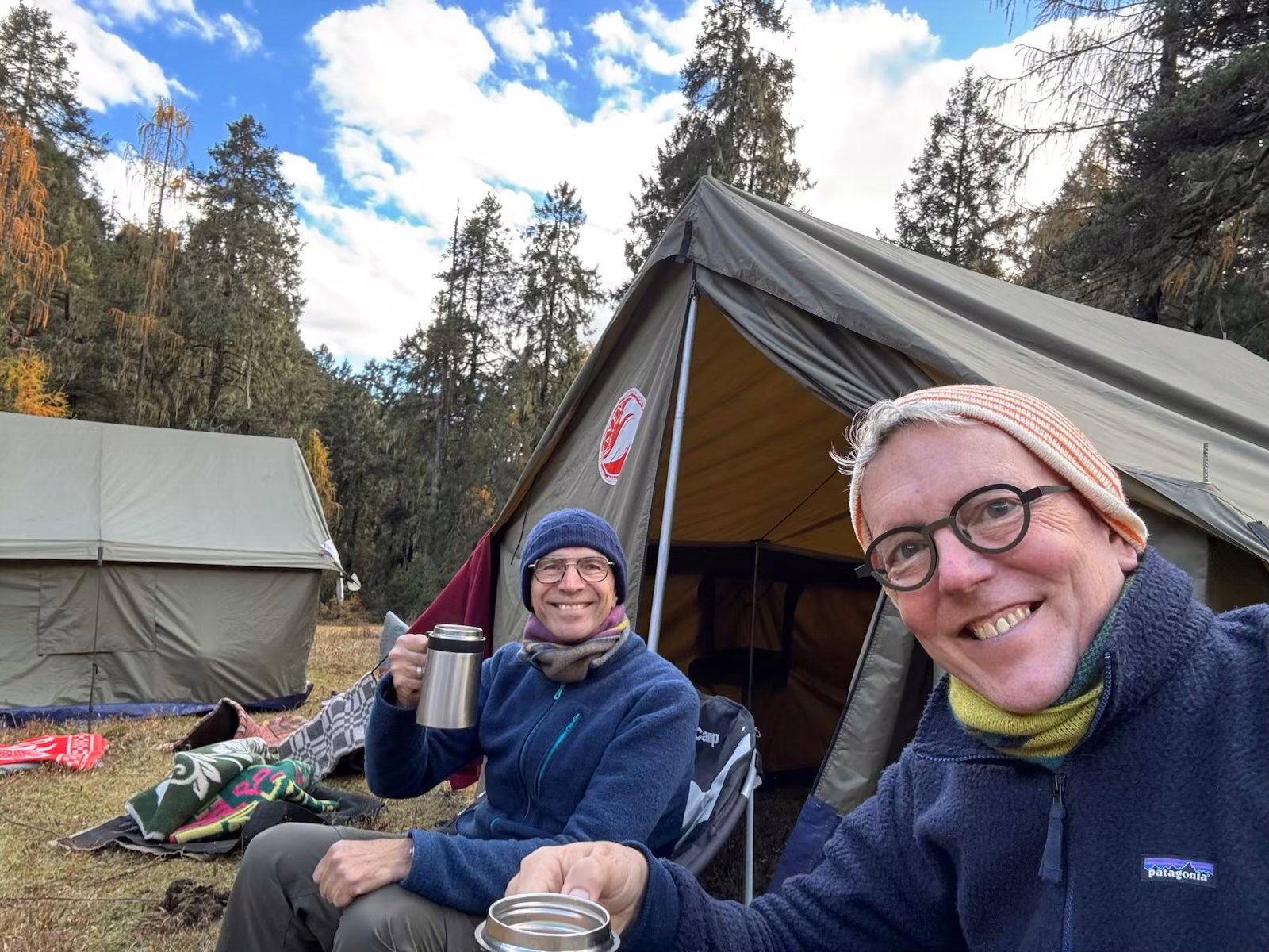 Guests relaxing with warm drinks beside canvas tents at Tshaluna forest camp, Bhutan.