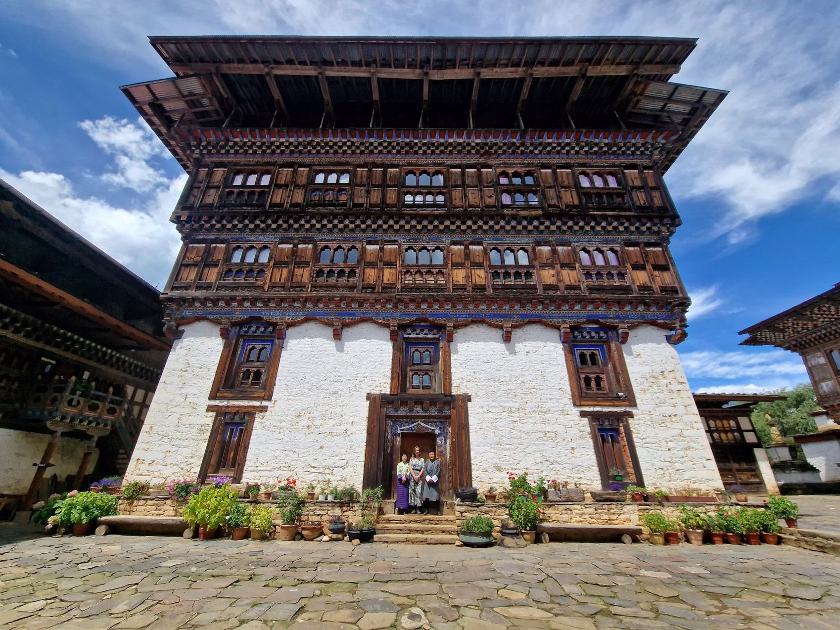 Ogyen Choling heritage house in Tang Valley, Bumthang, with visitors at the entrance and flowers lining the courtyard.