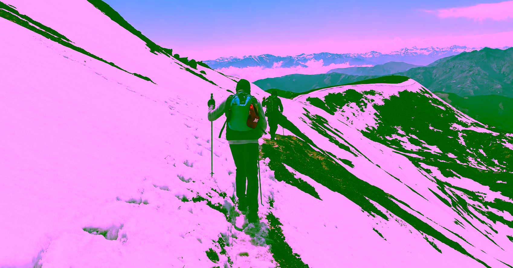 Two trekkers follow a snowy ridge on the Nub Tshonapata trail, with distant Himalayan peaks beyond.