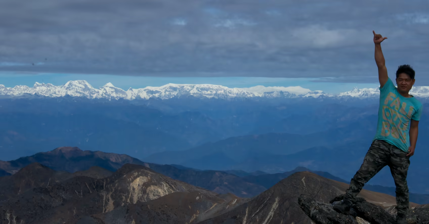 A trekker on a rocky Dagala viewpoint with distant Himalayan mountains.