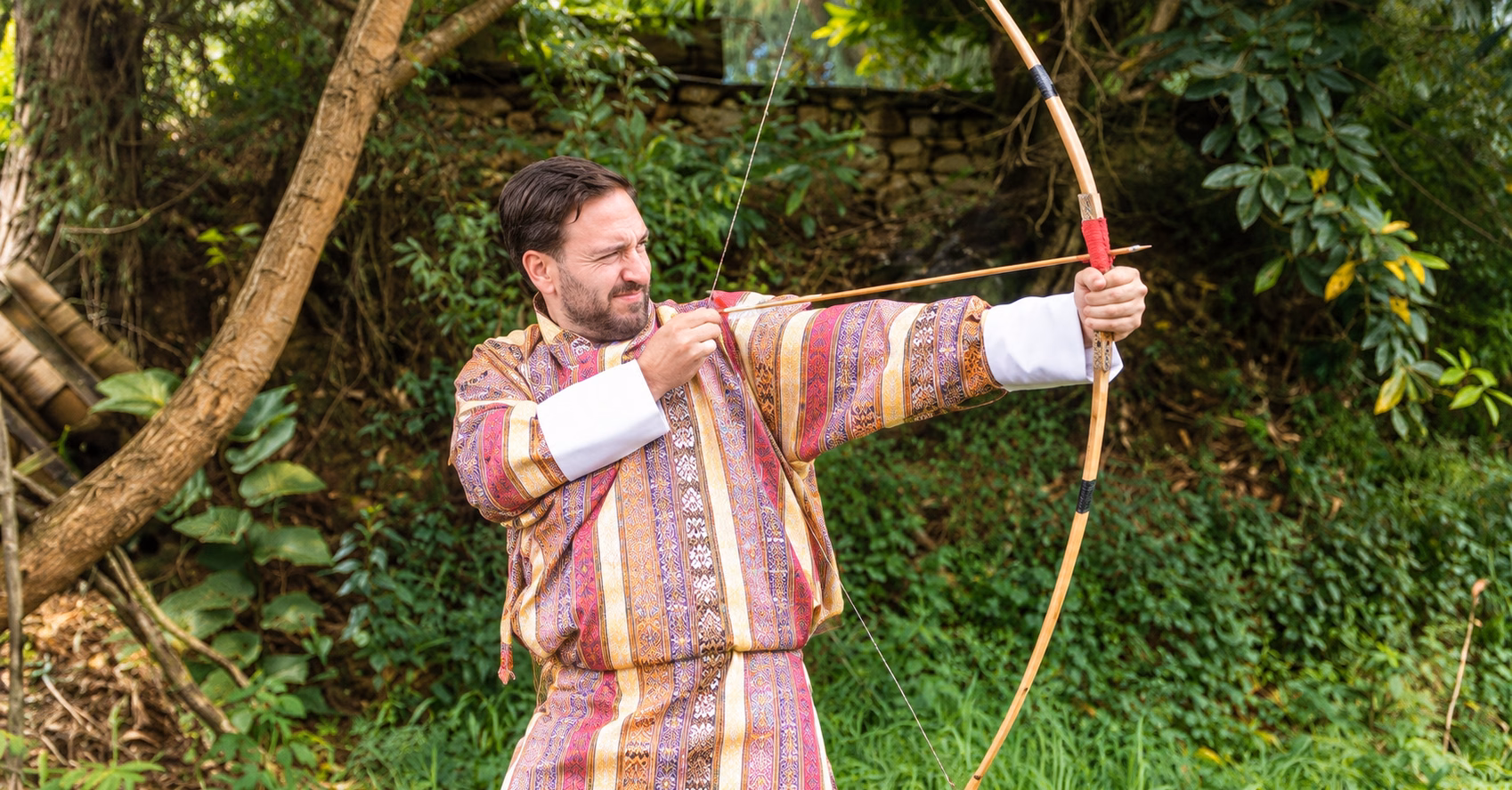 Guest wearing a Bhutanese gho practising traditional archery during a farmhouse experience