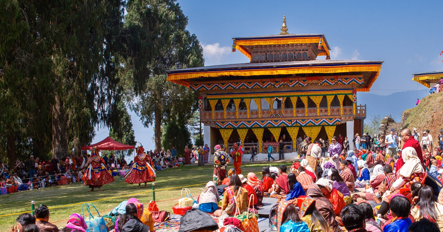Masked dancers performing before the temple and gathered spectators at Talo Tshechu in Bhutan