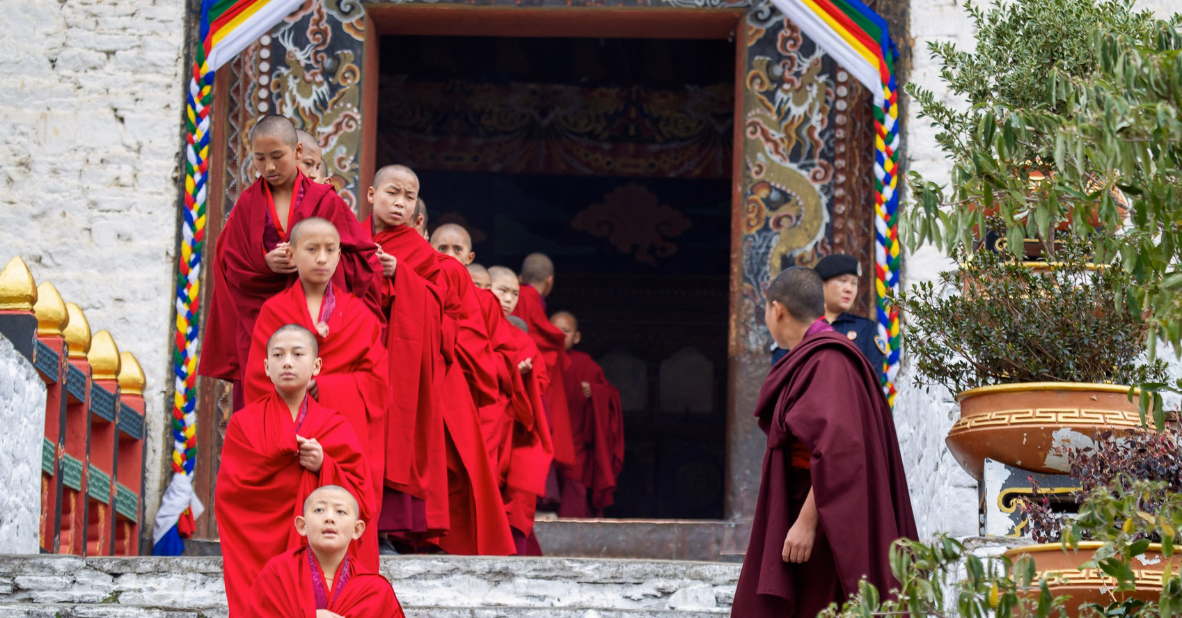 Monks in red robes descending decorated temple steps during Paro Tshechu in Bhutan