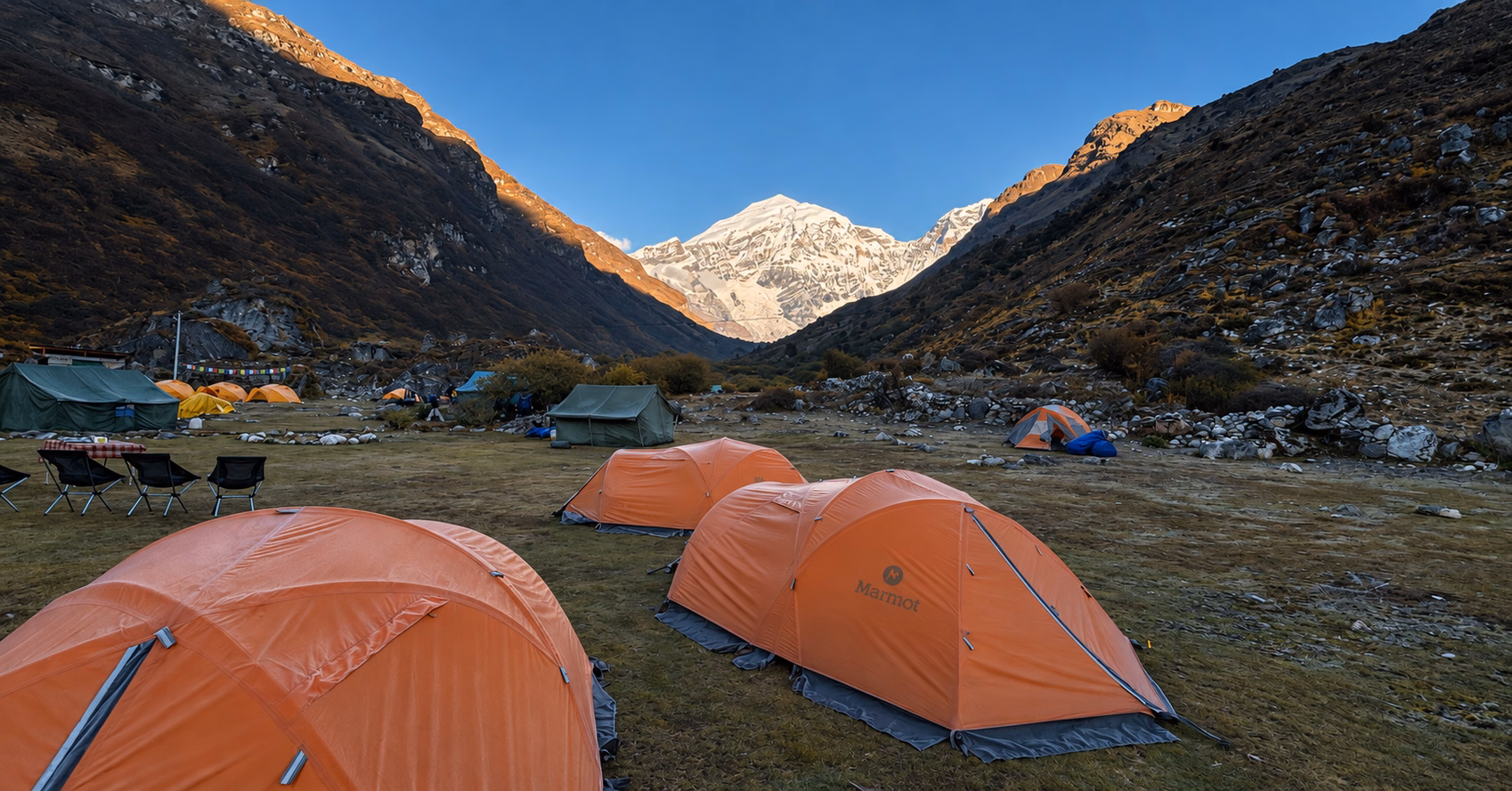 Orange trekking tents and camp chairs beneath snow-covered Jomolhari in Bhutan