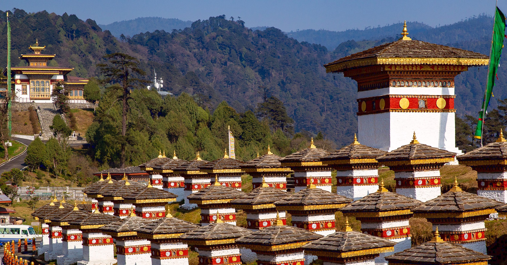 White and gold Druk Wangyal chortens at Dochula Pass against forested hills