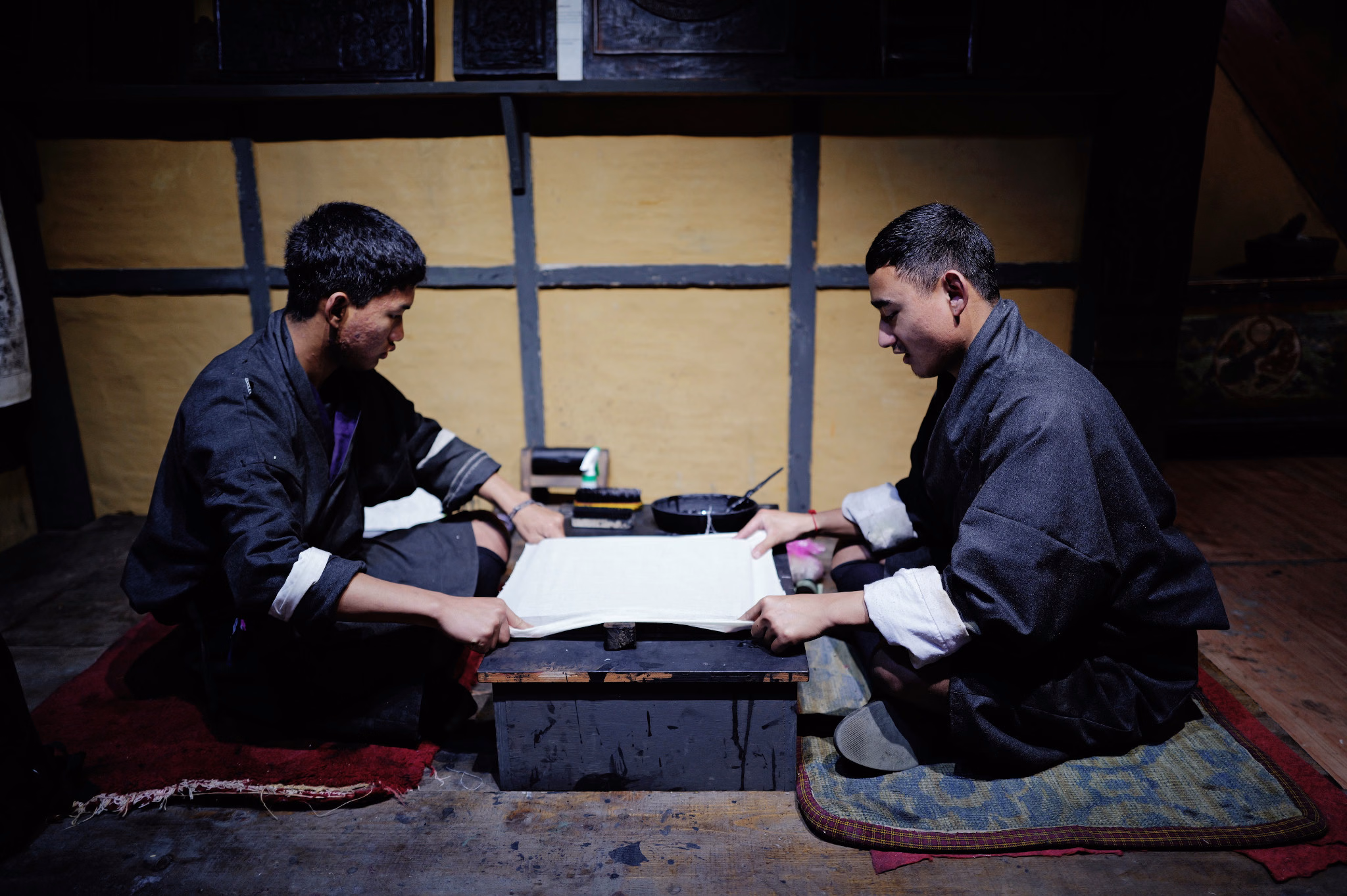 Two people in gho working together over a large sheet of paper in a traditional interior.