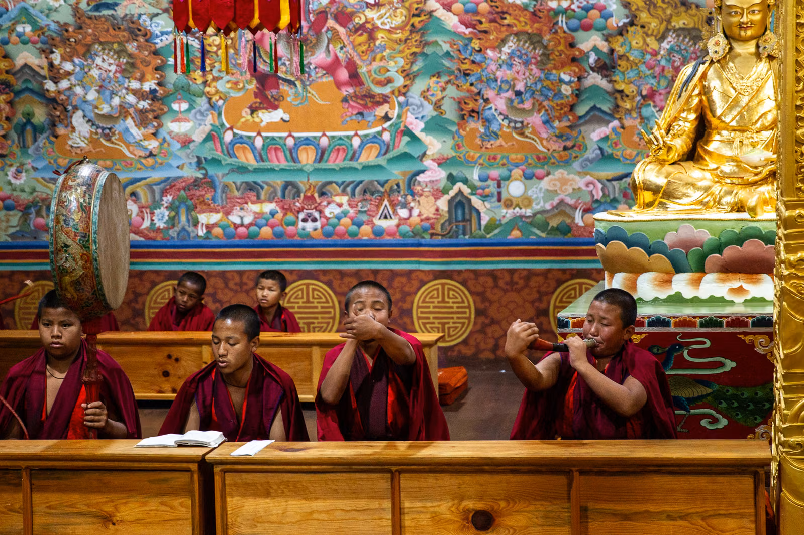Monks play ritual instruments inside a richly decorated temple.