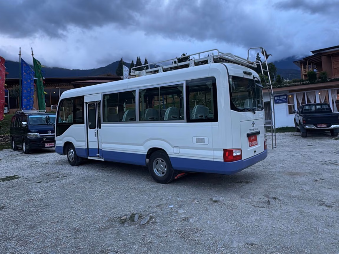 White and blue Toyota Coaster viewed from the rear and side.