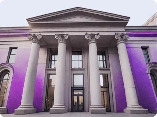Classical-style institutional building with tall Corinthian columns and arched windows. The exterior is lit with a gradient of purple lighting, giving it a modern, digital twist.