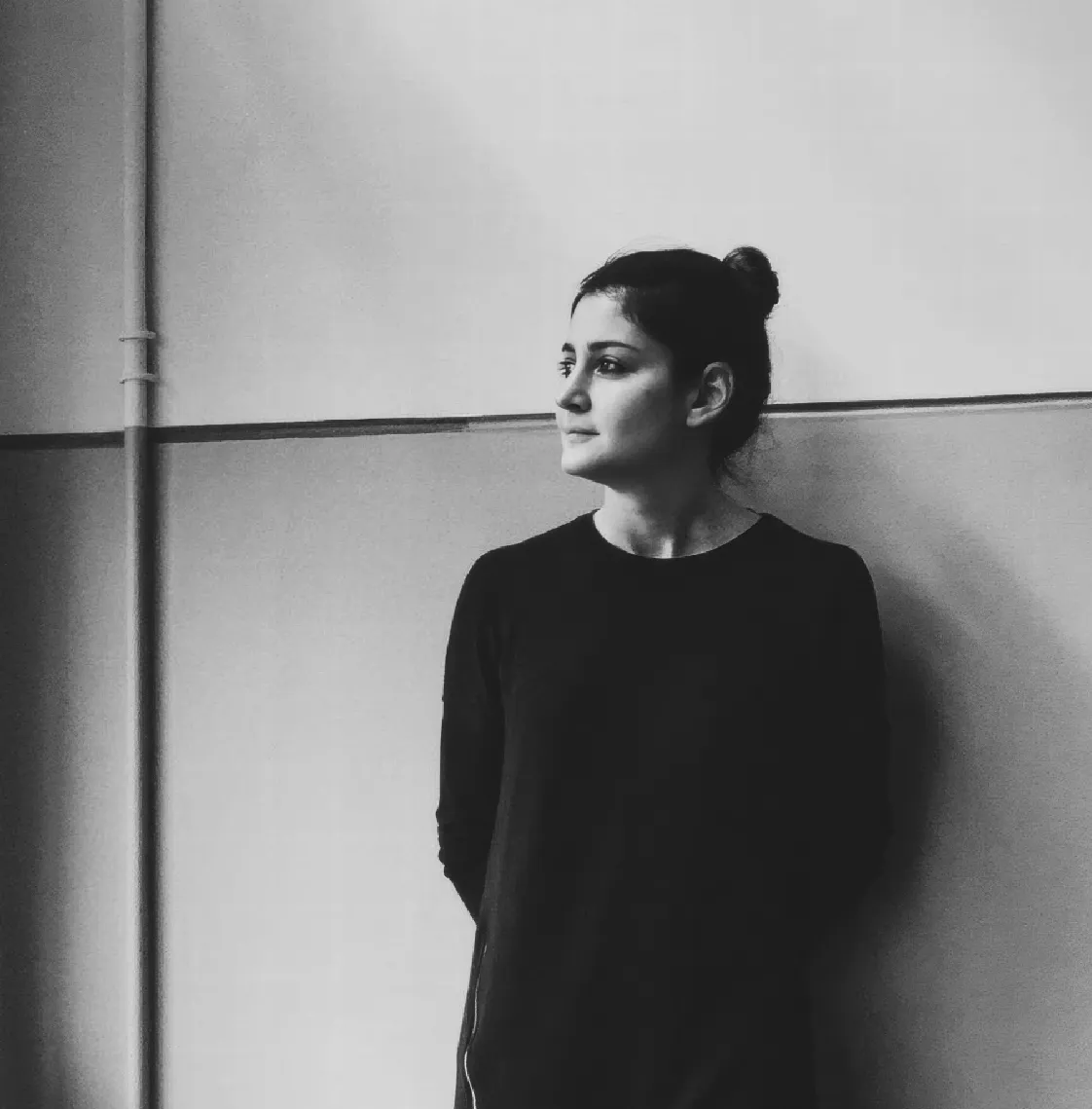 A black and white photo of a woman leaning against a wall.