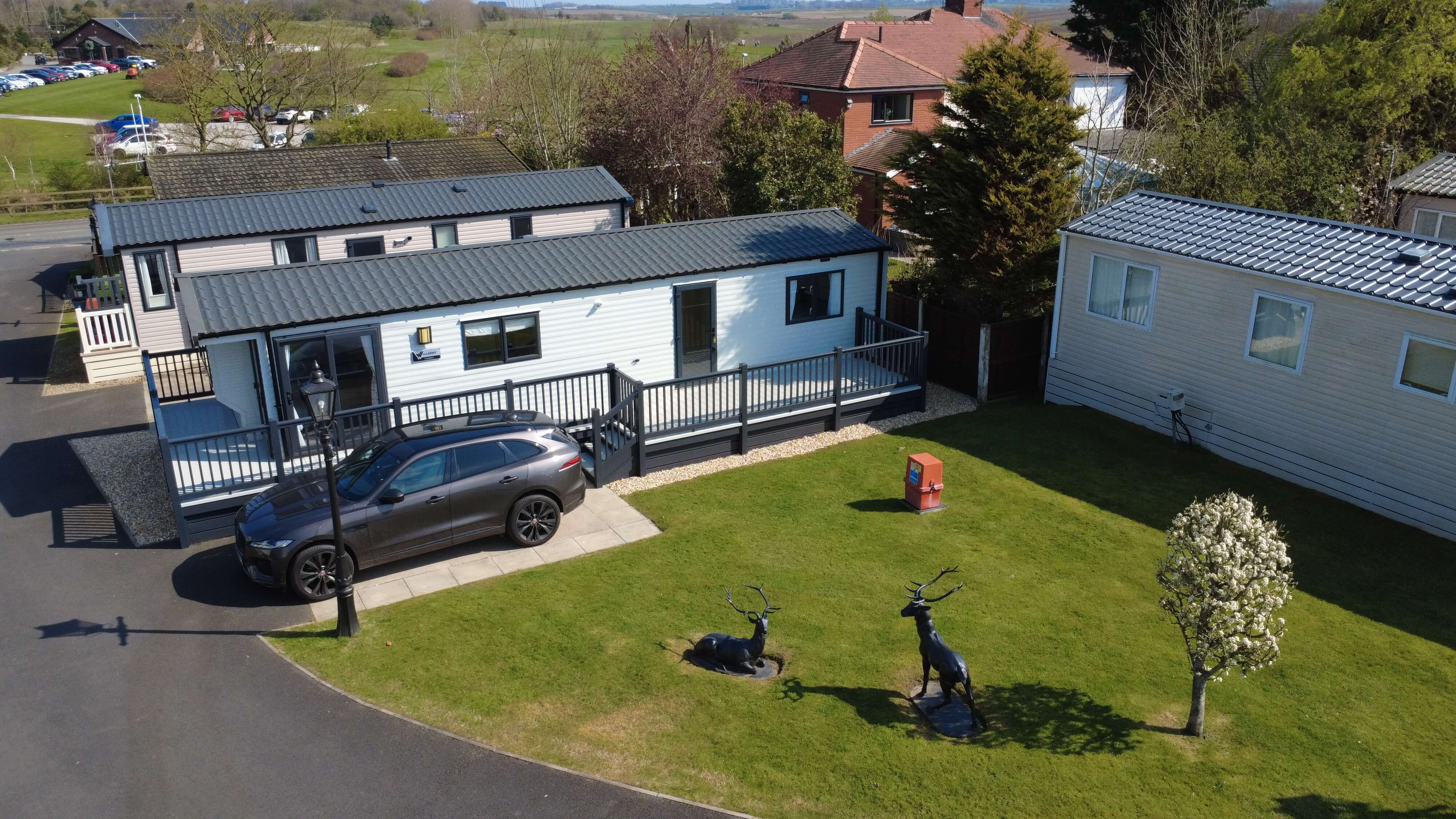 Mobile homes with deer statues on manicured lawn, parked car nearby