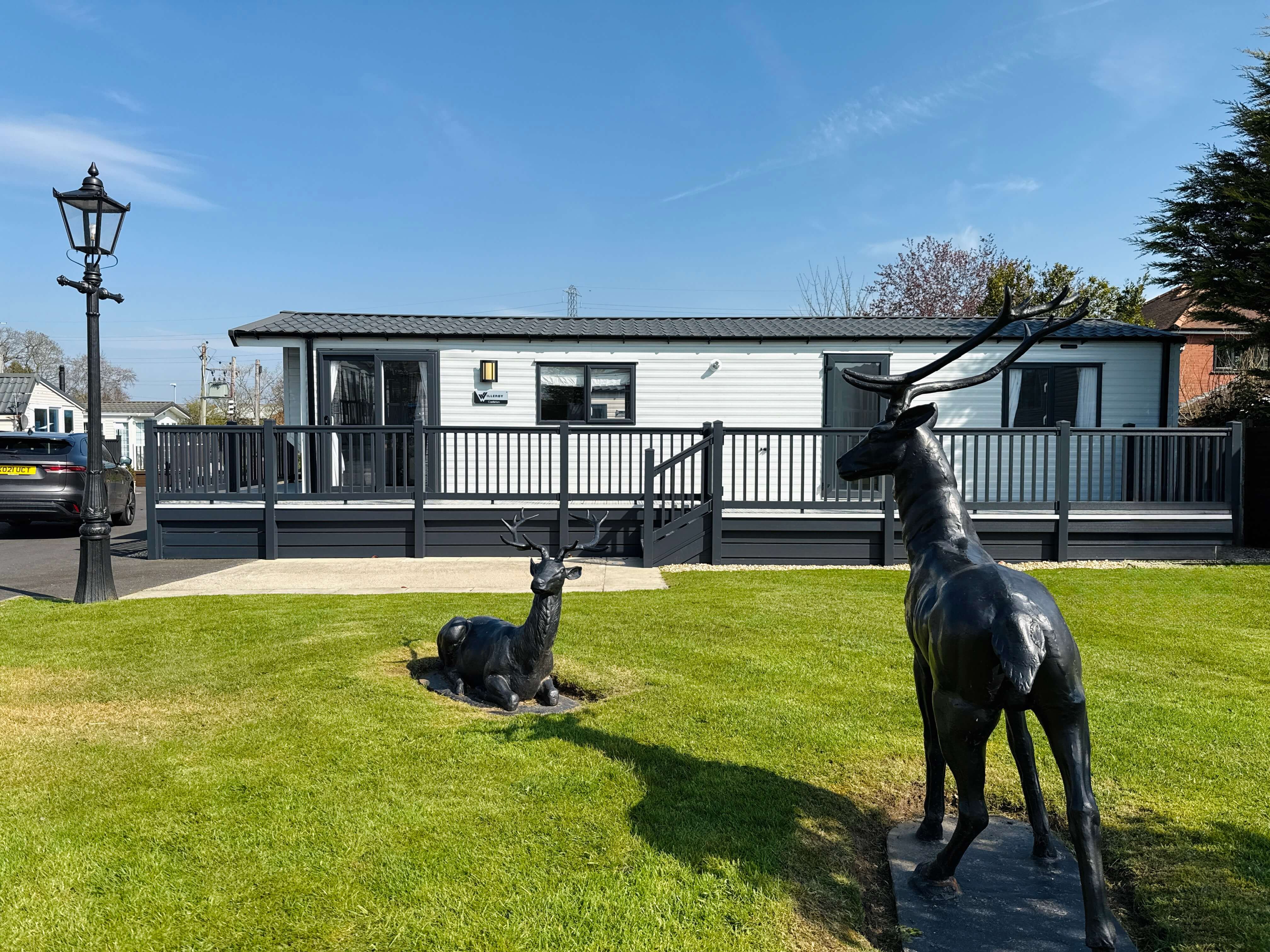 Two black deer statues on green lawn near white mobile home and lamp post