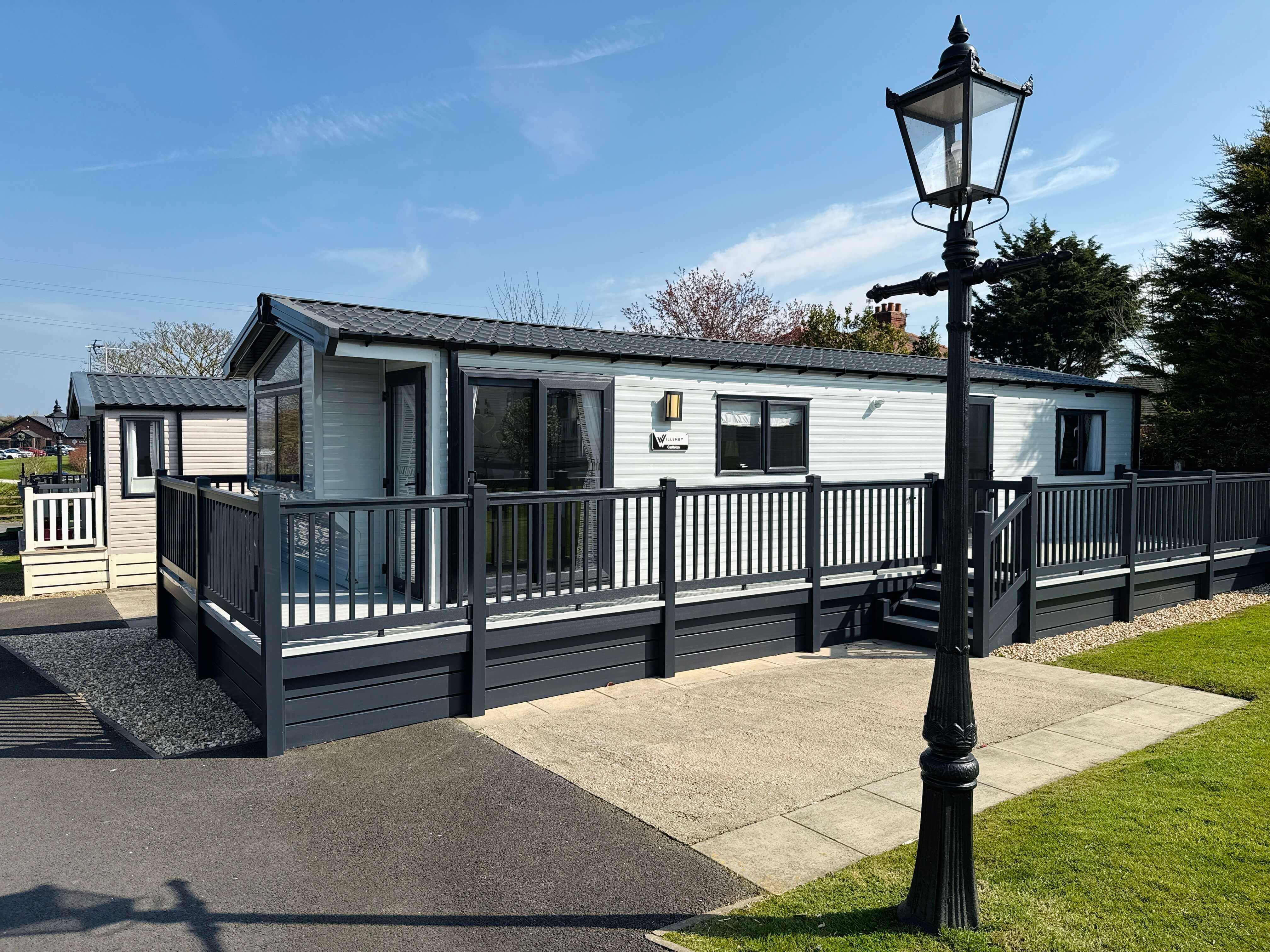Modern mobile home with dark railings and vintage street lamp on sunny day