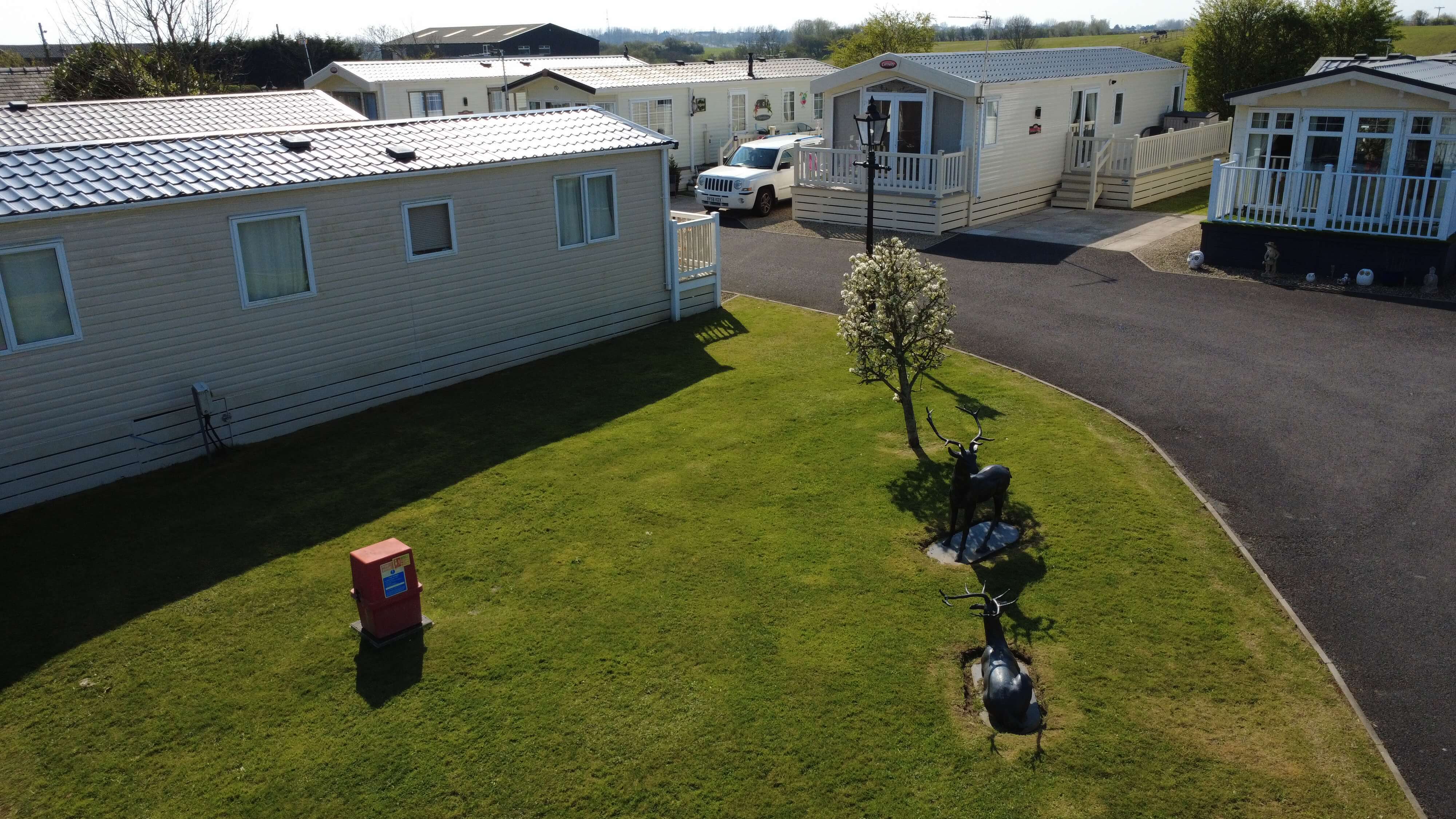 Mobile homes with manicured lawn, deer statue, and red utility box