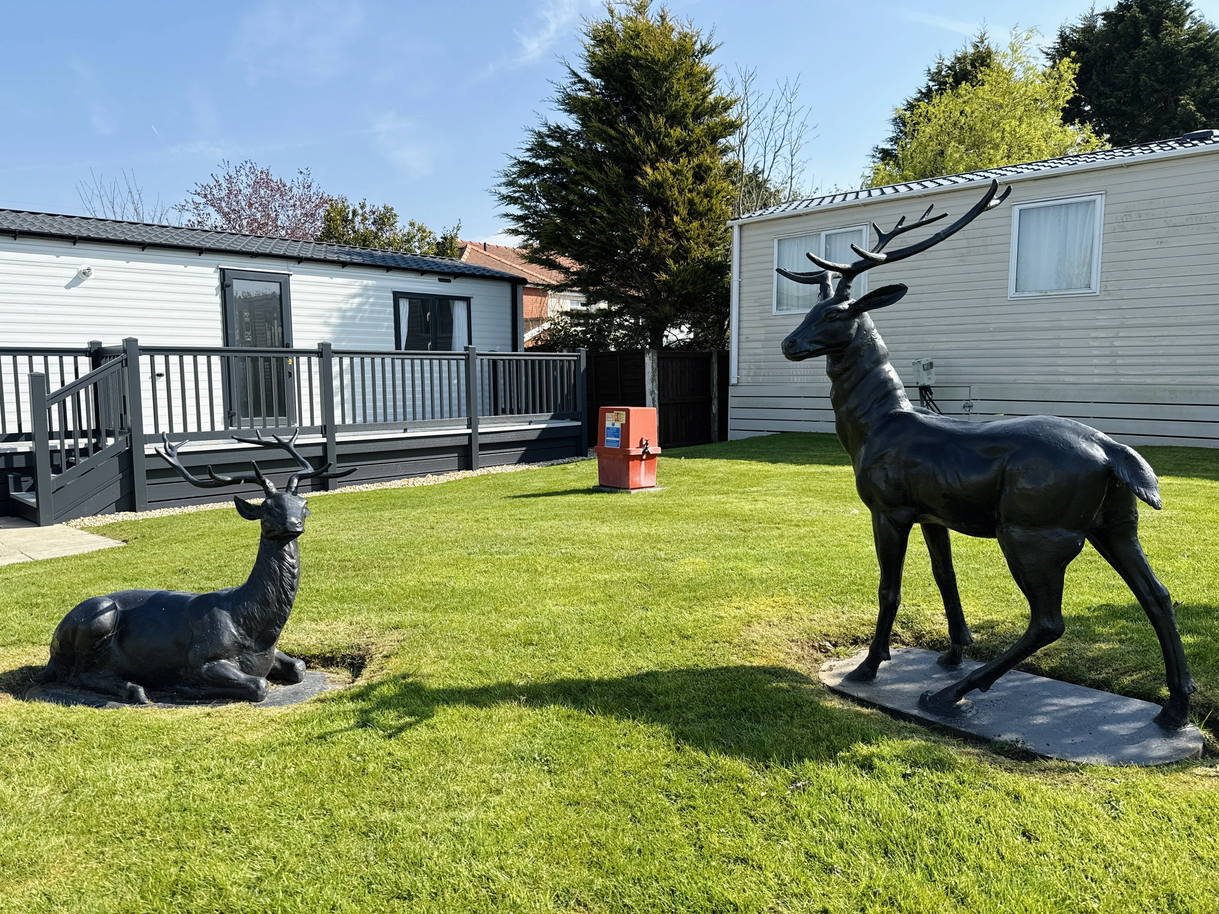 Two black deer statues on grass near mobile homes on sunny day