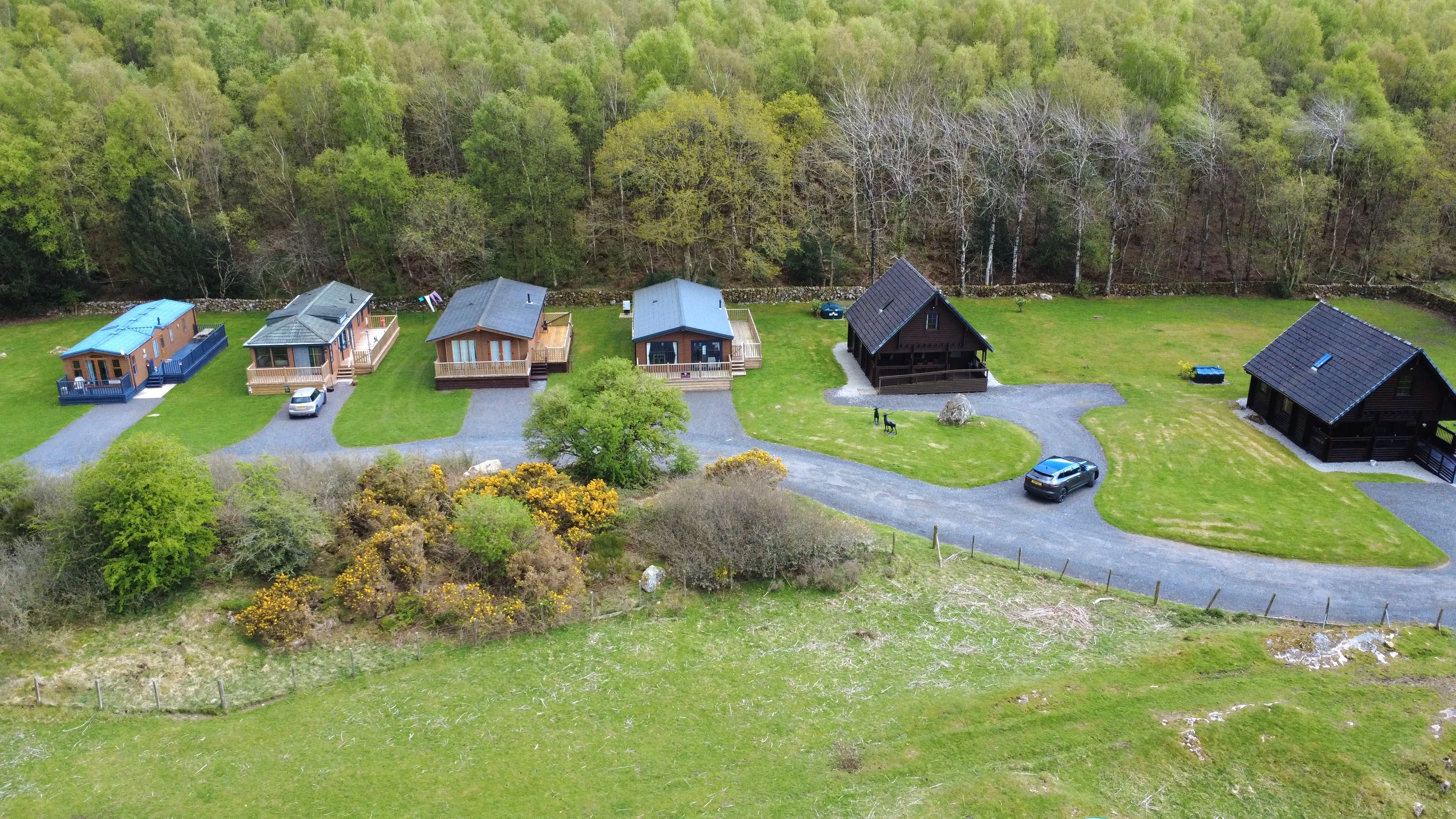 Aerial view of holiday cabins in a forested landscape with parked cars