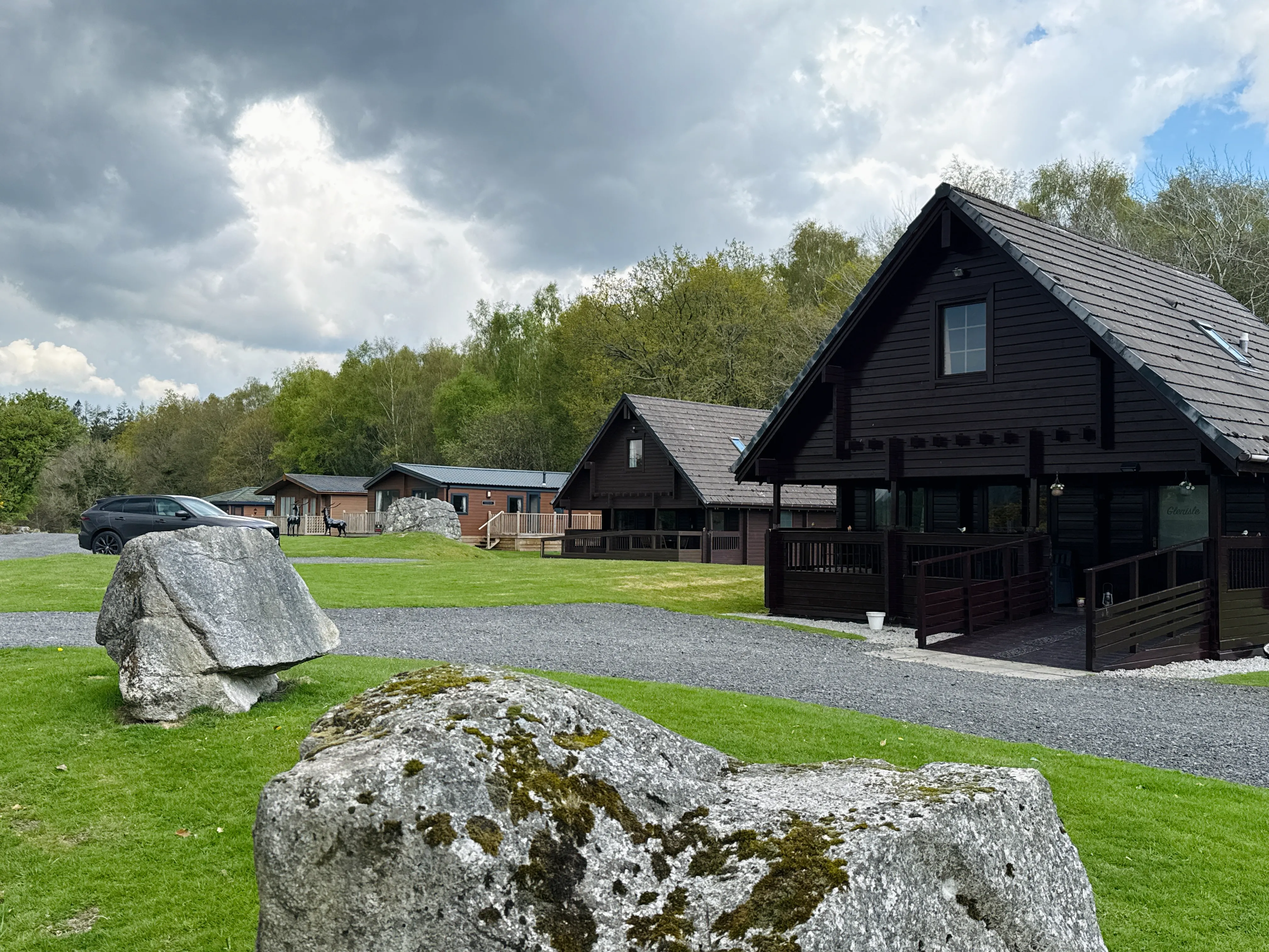 Dark wooden cabins with large rocks on grassy landscape under cloudy sky