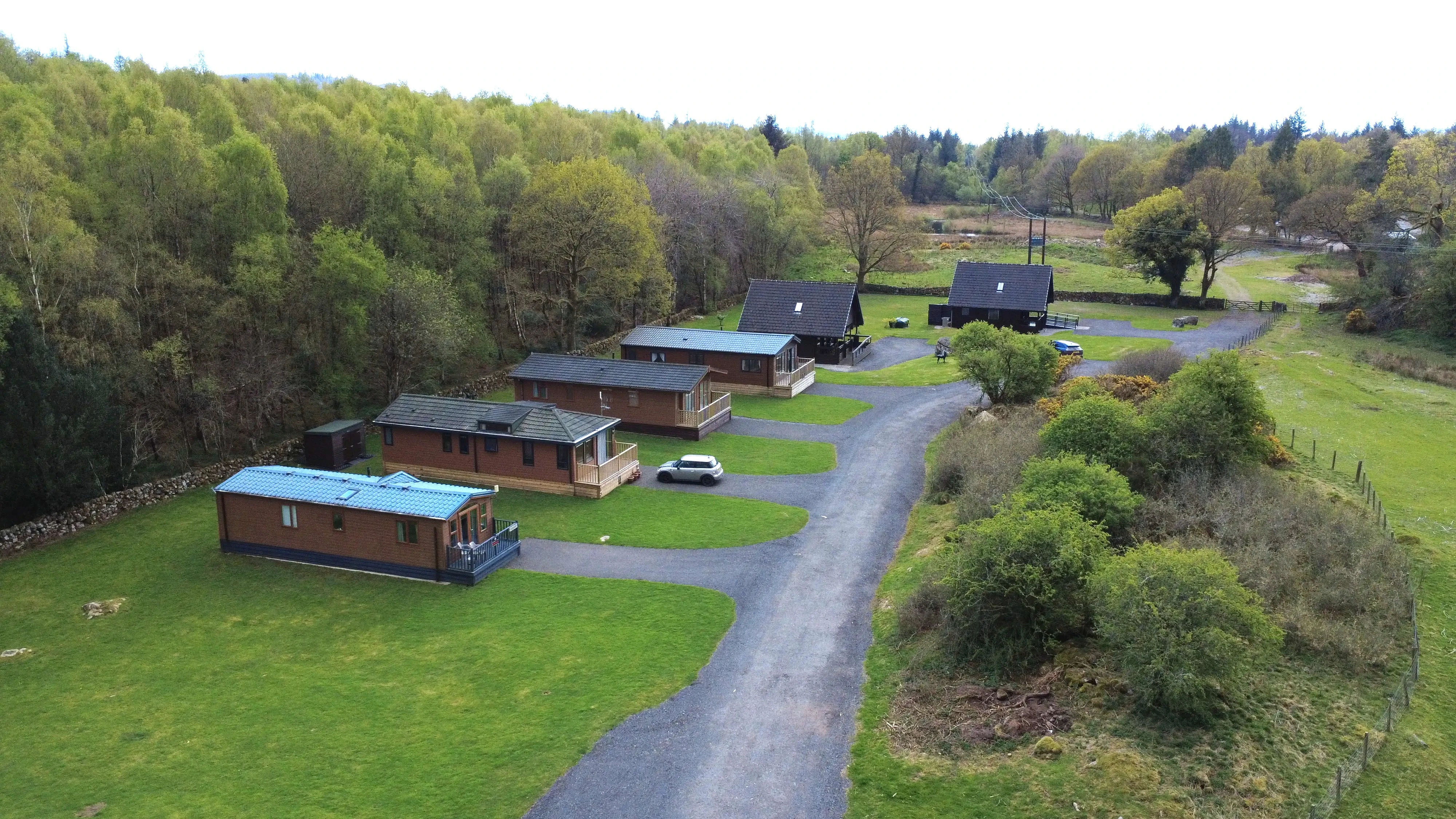 Aerial view of wooden cabins on winding road surrounded by lush green forest