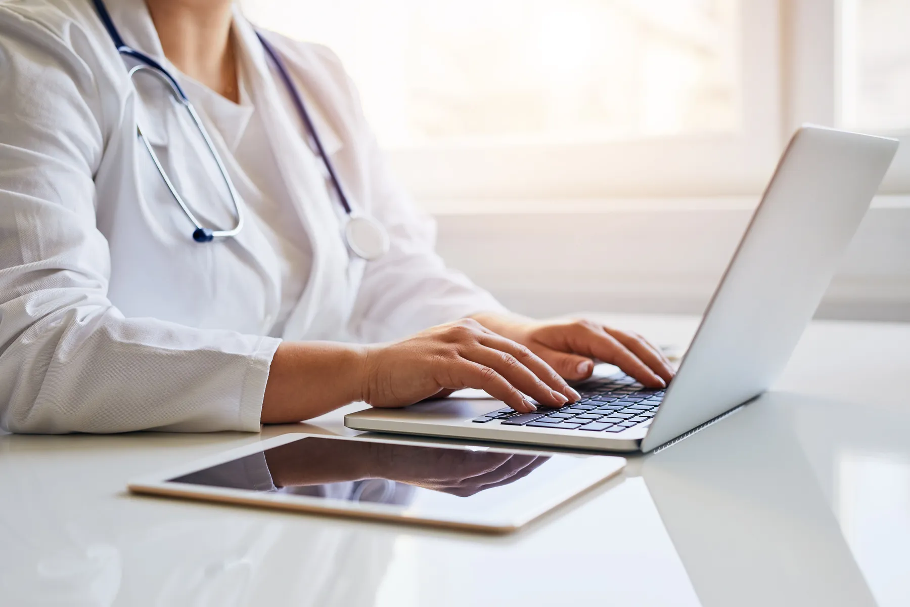 A woman with a stethoscope is typing on a laptop.