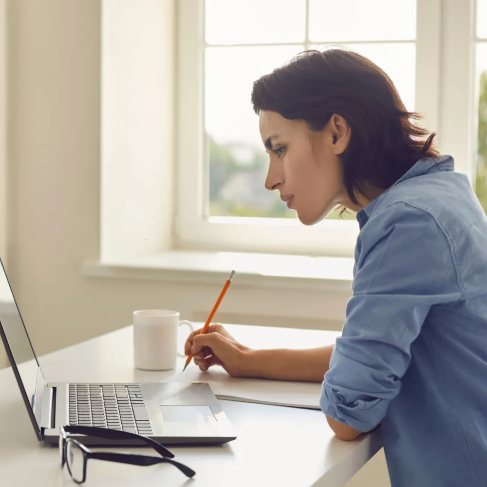 A woman sitting at a desk writing on a laptop.