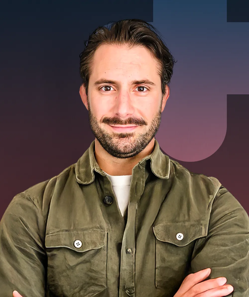 A man with his arms crossed in front of a purple background.