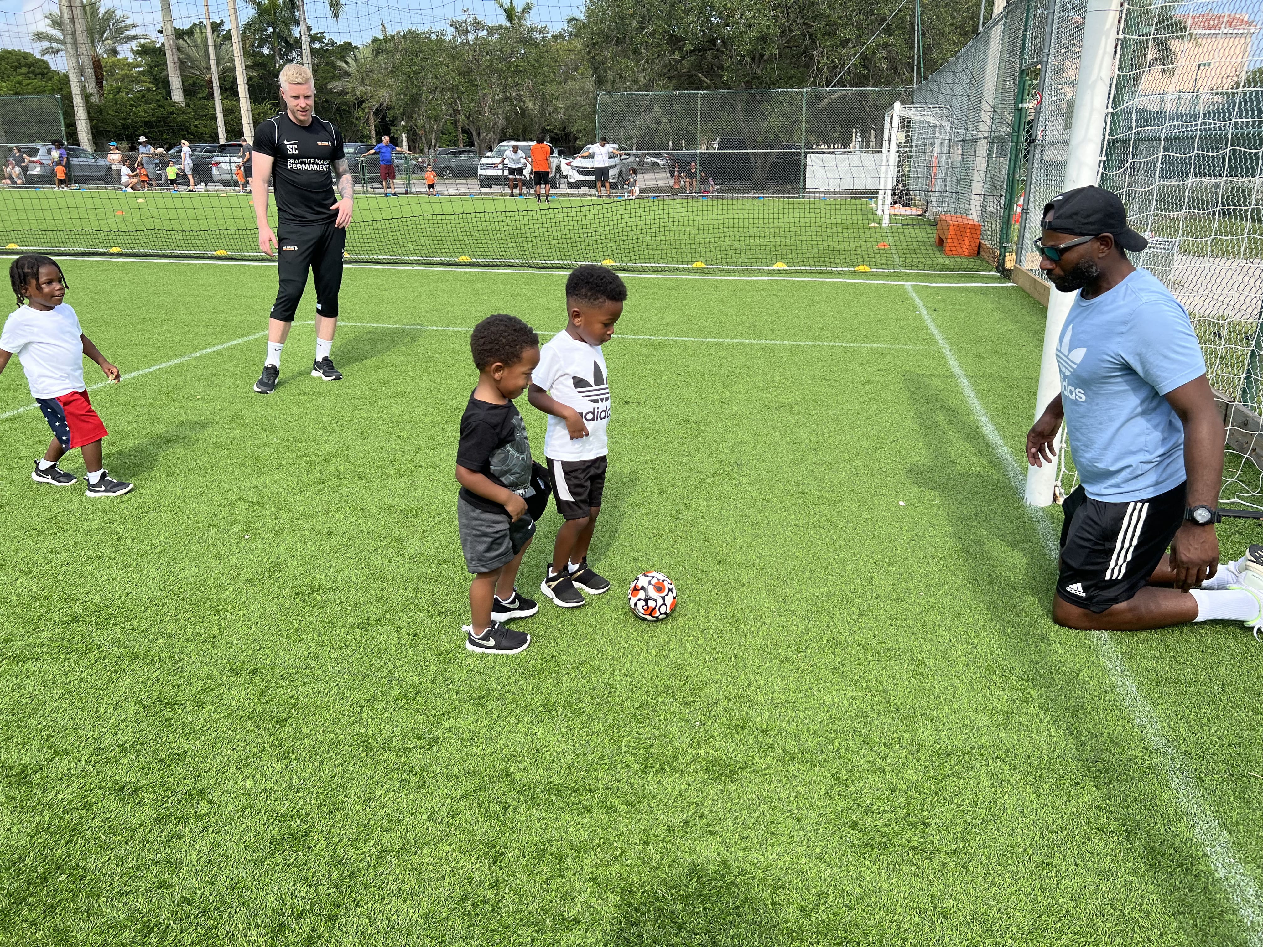 Kids chasing a soccer ball during outdoor training at youth soccer camp.