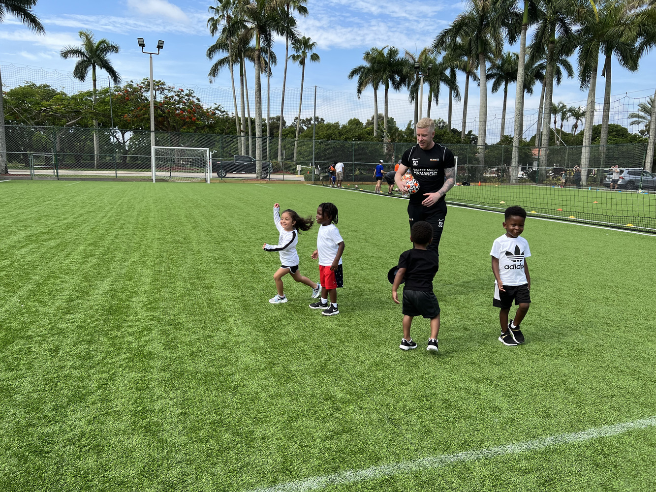 Young children playing soccer on a sunny field during early training session.