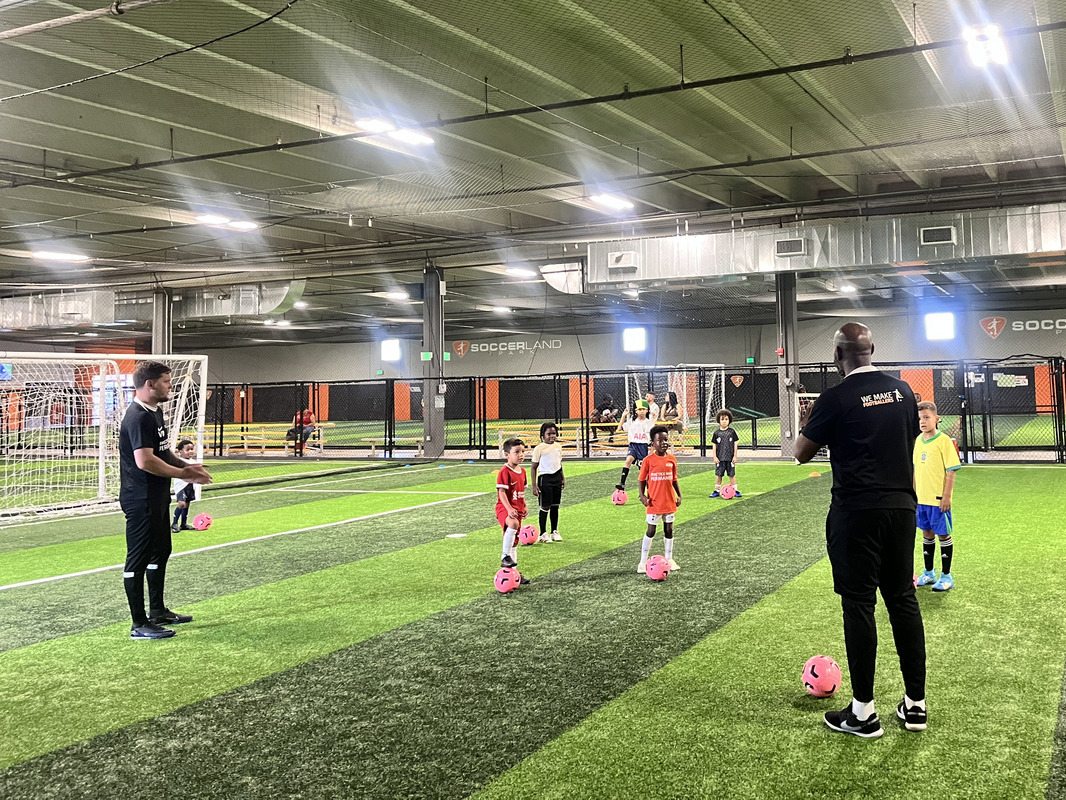 Coach encouraging early soccer learners during skill-building activity.