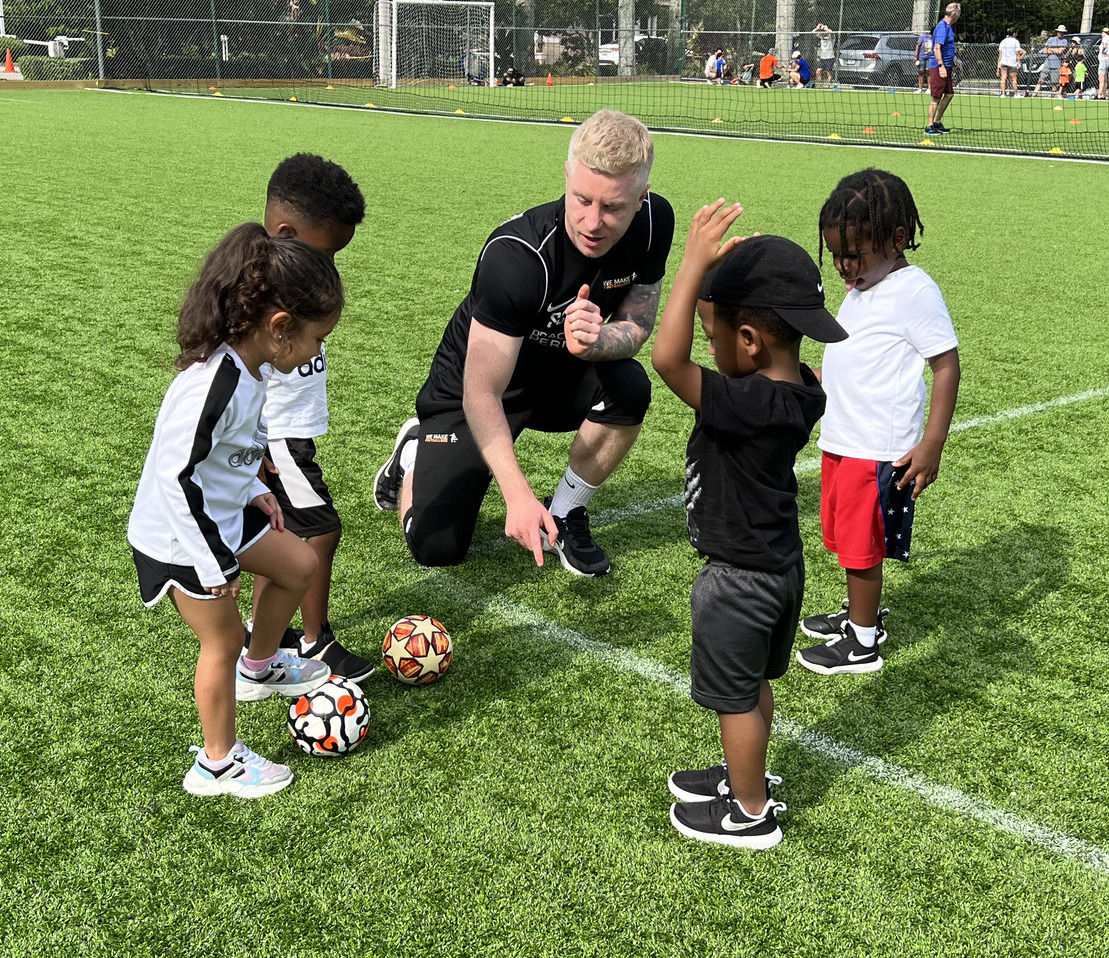 Young children aged 4–6 engaged in playful soccer drills with cones.