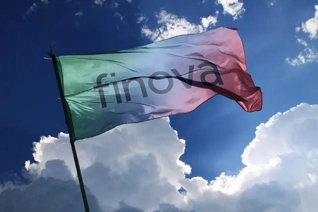 Finova branding flag, green-blue-red gradient, waves against a sunny blue sky with clouds.