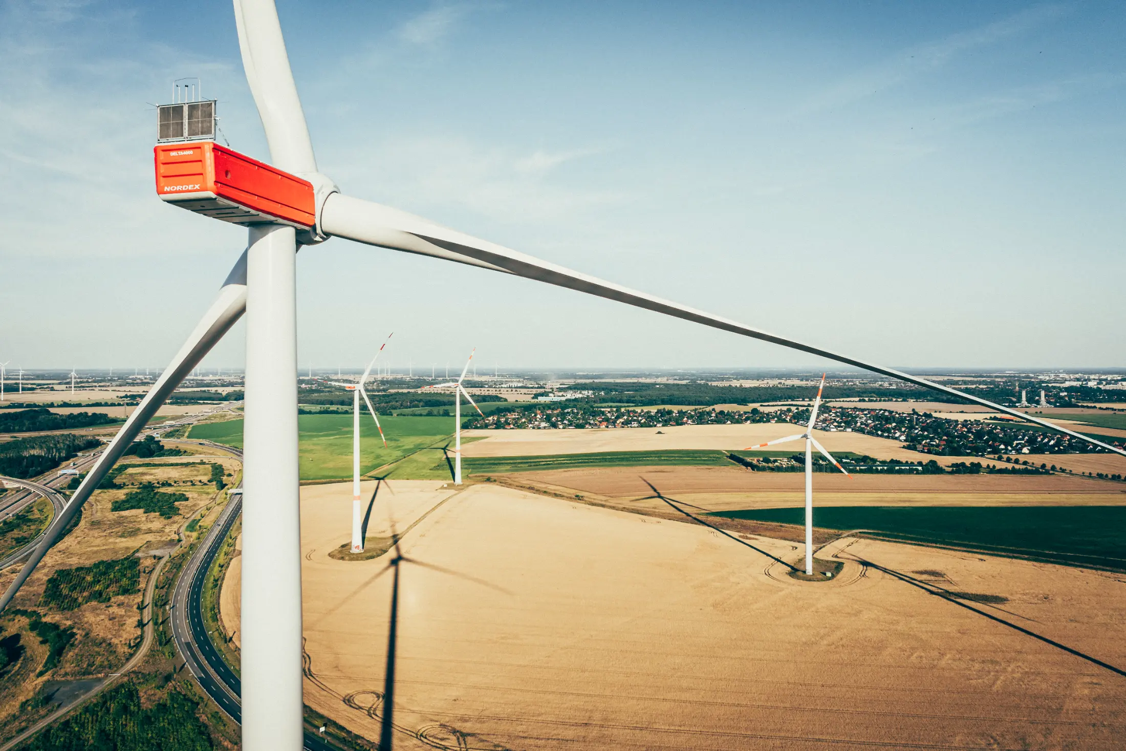 Eine hochauflösende Drohnenaufnahme mit mehreren Windkraftanlagen auf Feldern. 