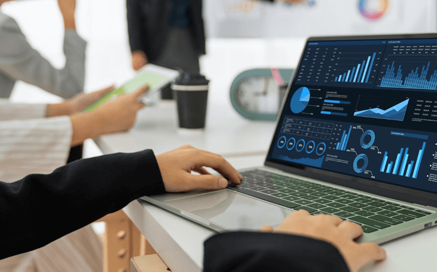 Hands typing on a laptop showing data analytics and graphs on the screen.
