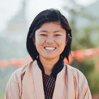 Smiling portrait of Nim Dem, Raven guide in traditional kira, embodying hospitality and joy.