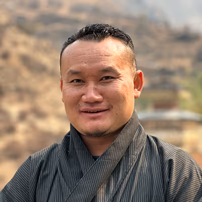 Portrait of Punap, Raven guide in striped gho, smiling warmly against a mountain backdrop.