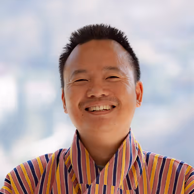 Portrait of Jiwan, Raven chauffeur in striped gho, radiating warmth and cheerful hospitality.