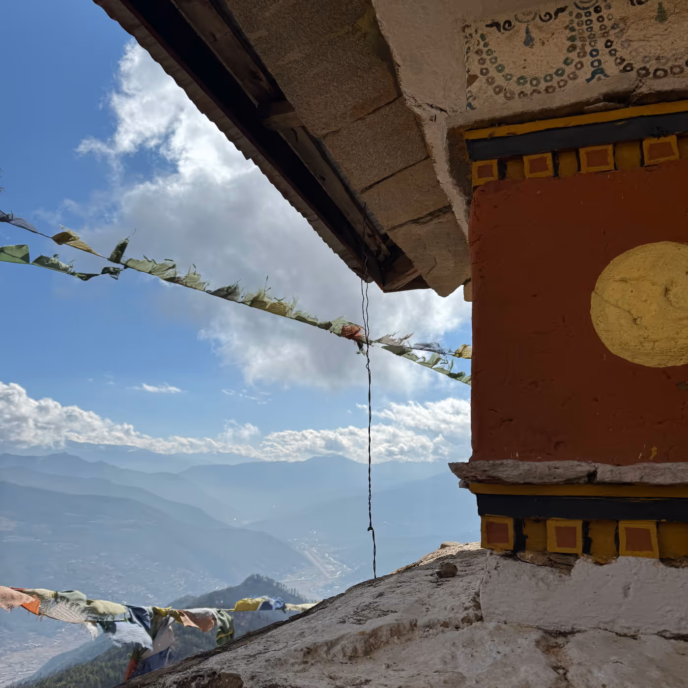 Looking out from a monastery wall near Bumdra, prayer flags flutter above the Paro valley under a brilliant sky of clouds and sun.
