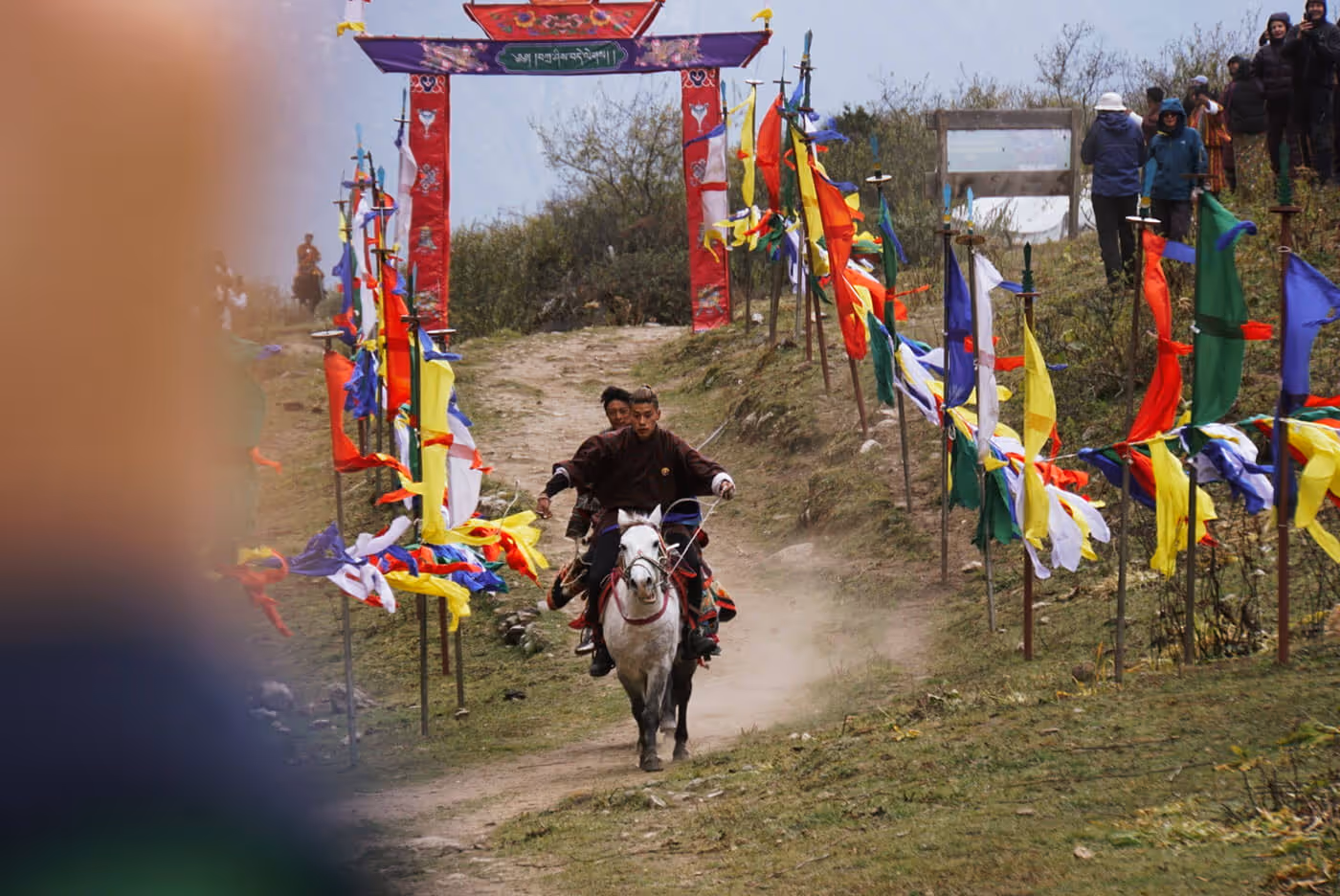 Young Bhutanese horsemen galloping through a corridor of prayer flags during the Jumolhari Mountain Festival games.
