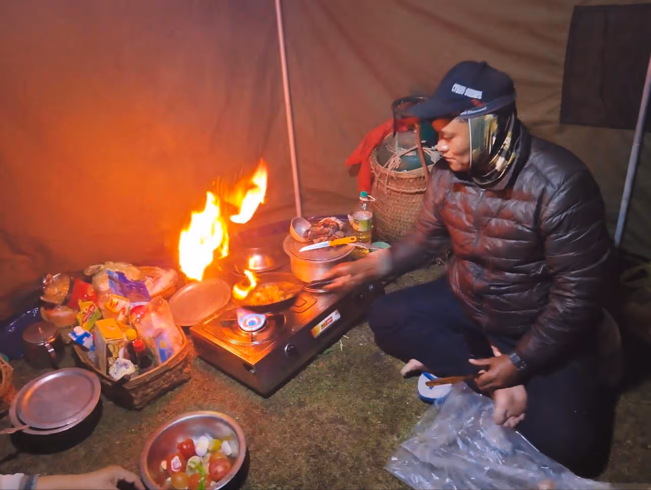 Camp chef preparing a hot meal over open flame inside a cozy mess tent, bringing warmth and flavor to the high-altitude trek.