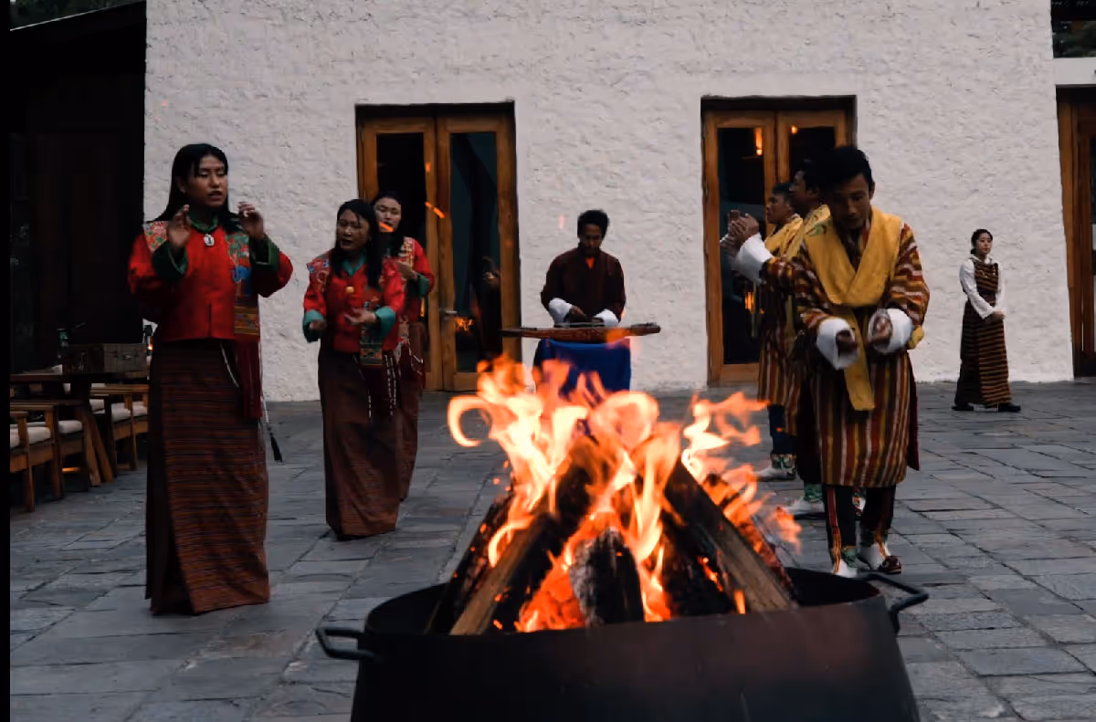 A lively Bhutanese cultural performance unfolds around a blazing fire pit as guests enjoy music, dance, and warm hospitality.
