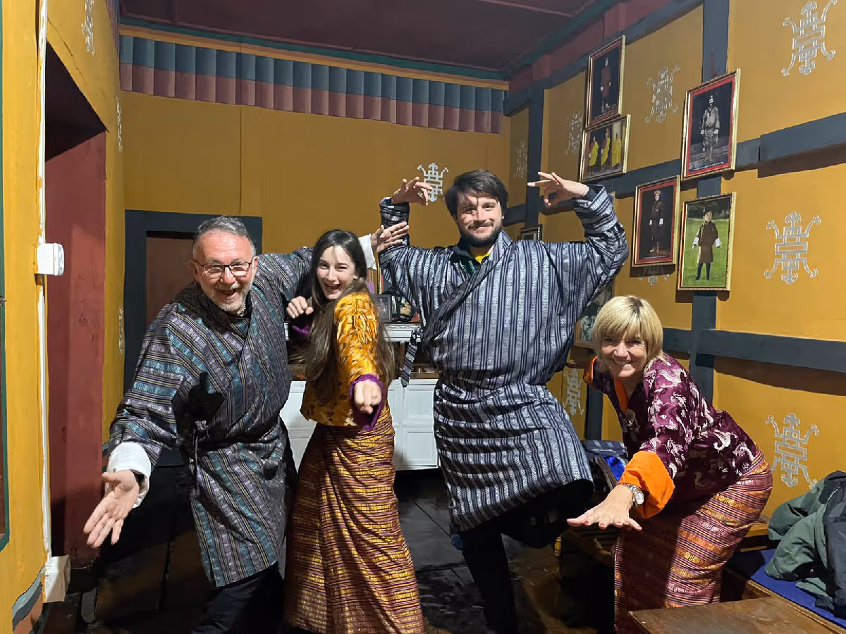 A joyful group of four travelers strike playful poses in a traditional Bhutanese room, dressed in vibrant gho and kira.