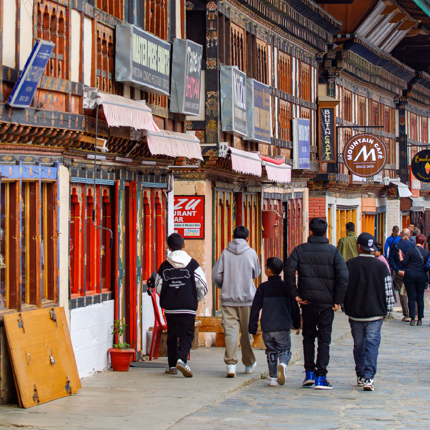 A group of Bhutanese youths stroll past traditional wooden storefronts along Paro’s pedestrian-friendly main street, where old-world charm blends with daily life.