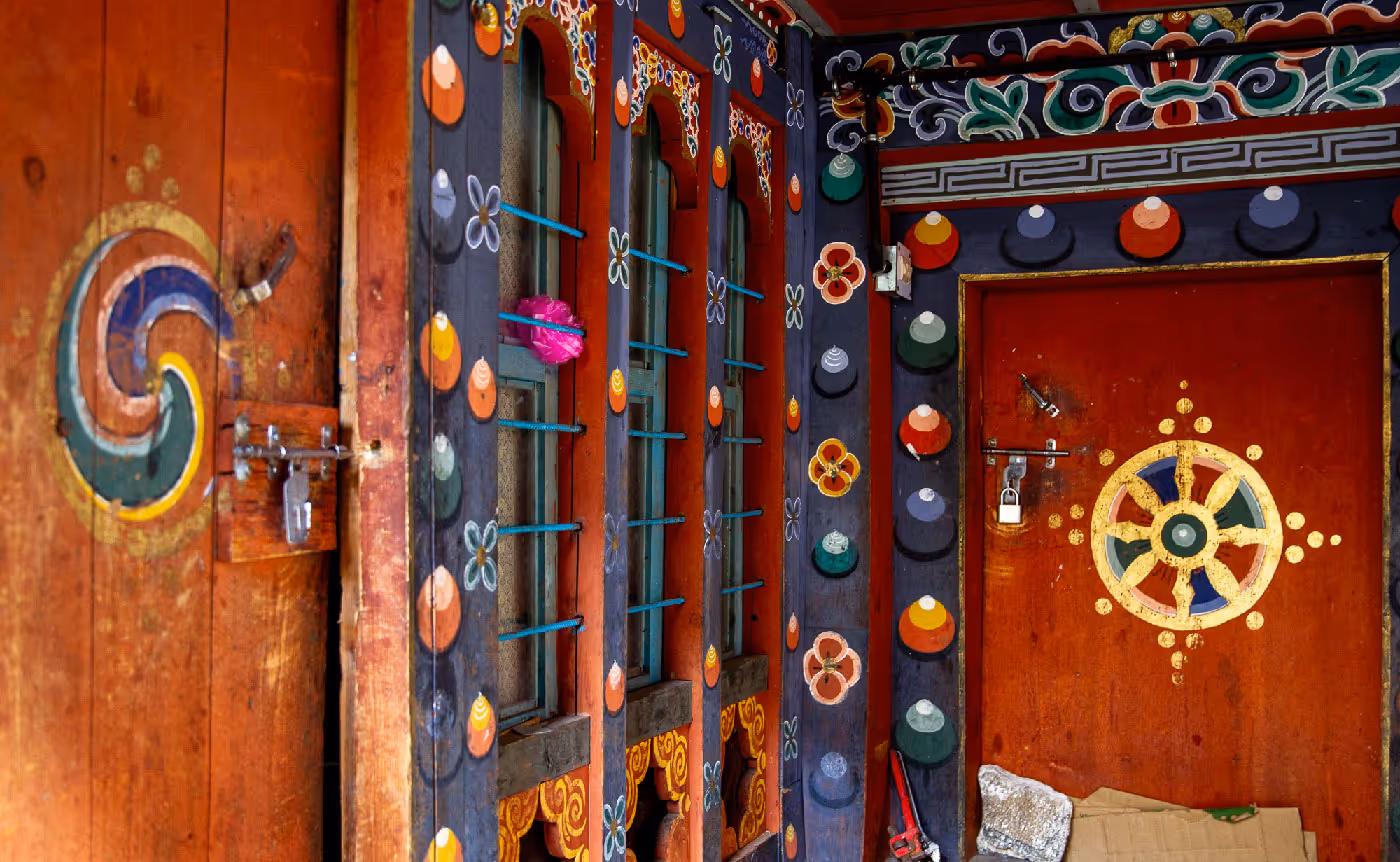 Vibrantly painted wooden window frames and door with floral and geometric motifs, capturing the colorful artistry of Bhutanese monastic design.