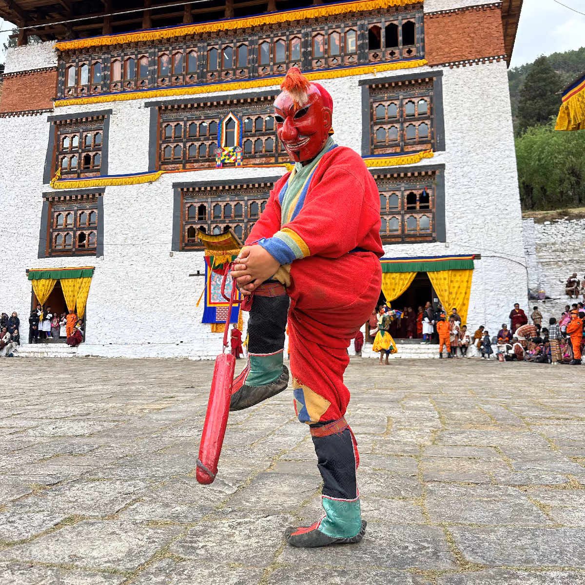 A festival clown (Atsara) in a red mask and boots entertains crowds in front of Paro Rinpung Dzong’s majestic facade.
