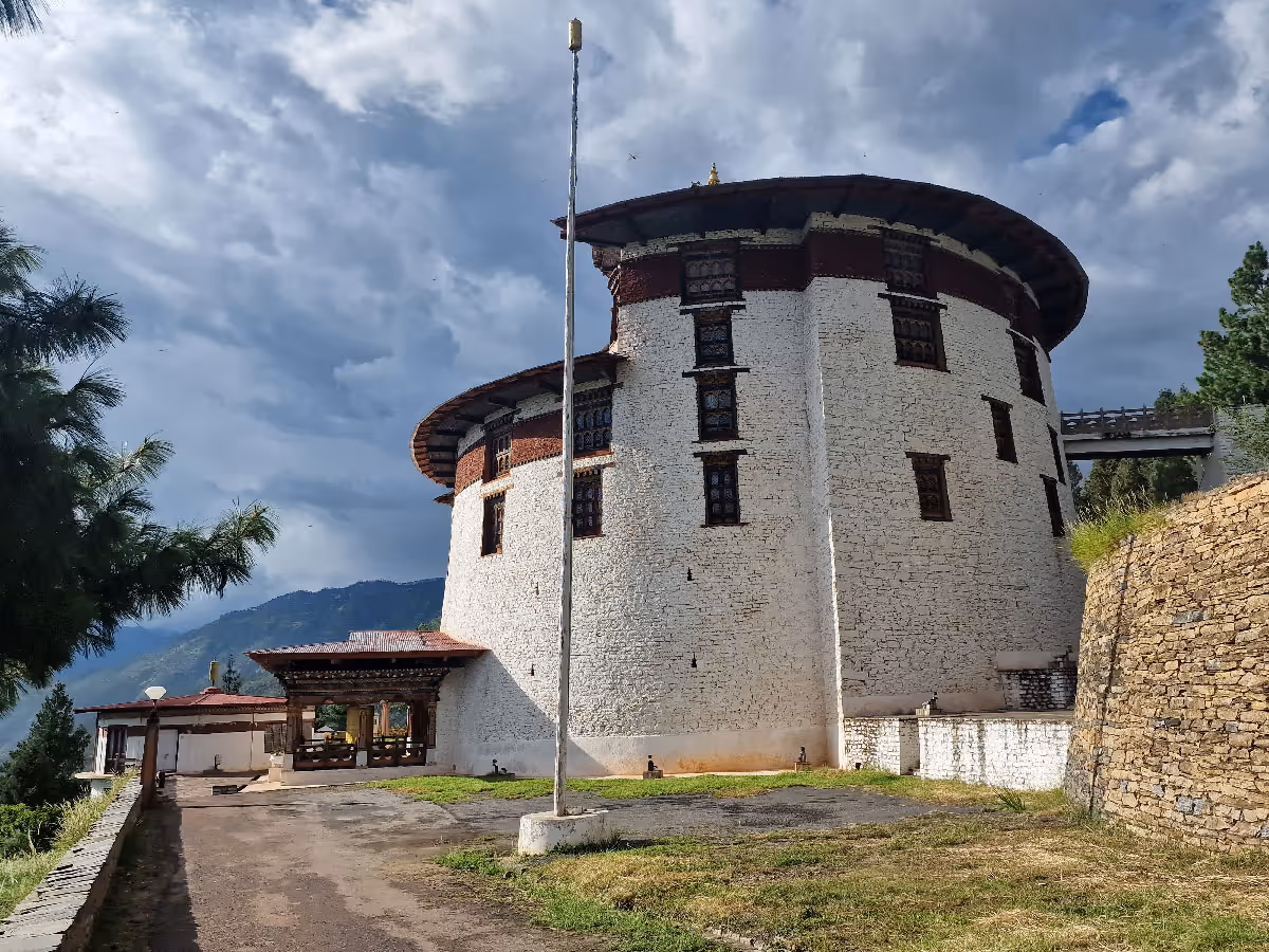 Imposing whitewashed walls of the Paro National Museum seen from below, with traditional Bhutanese windows and a cloudy sky adding contrast.