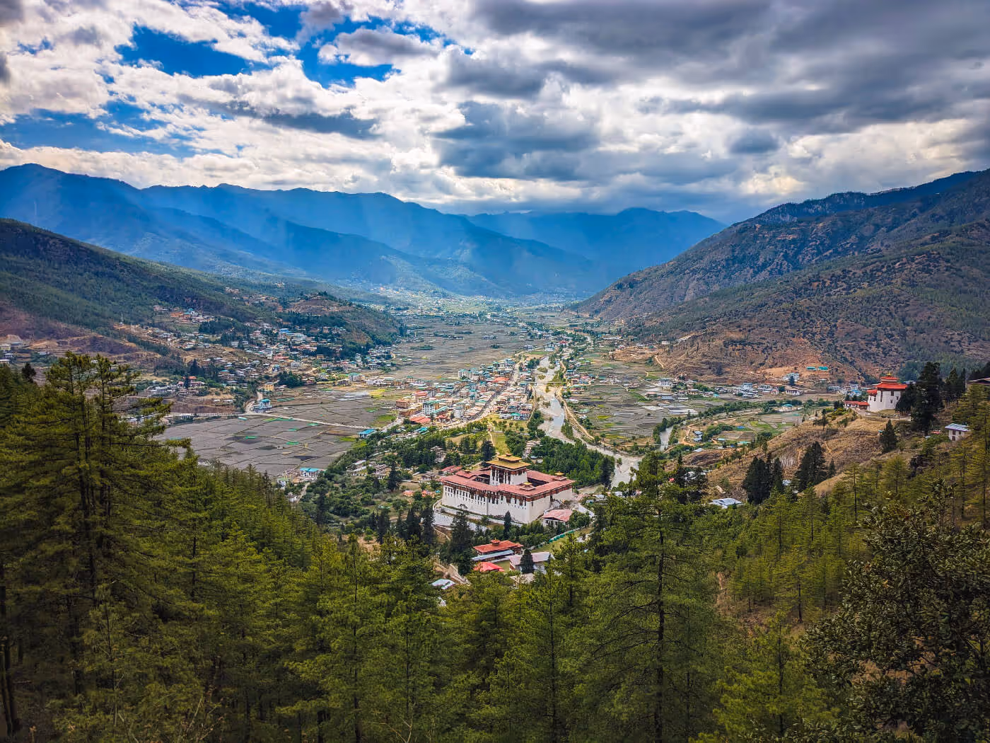 Aerial view of Paro Valley in Bhutan with Rinpung Dzong and terraced fields, framed by distant blue mountains.