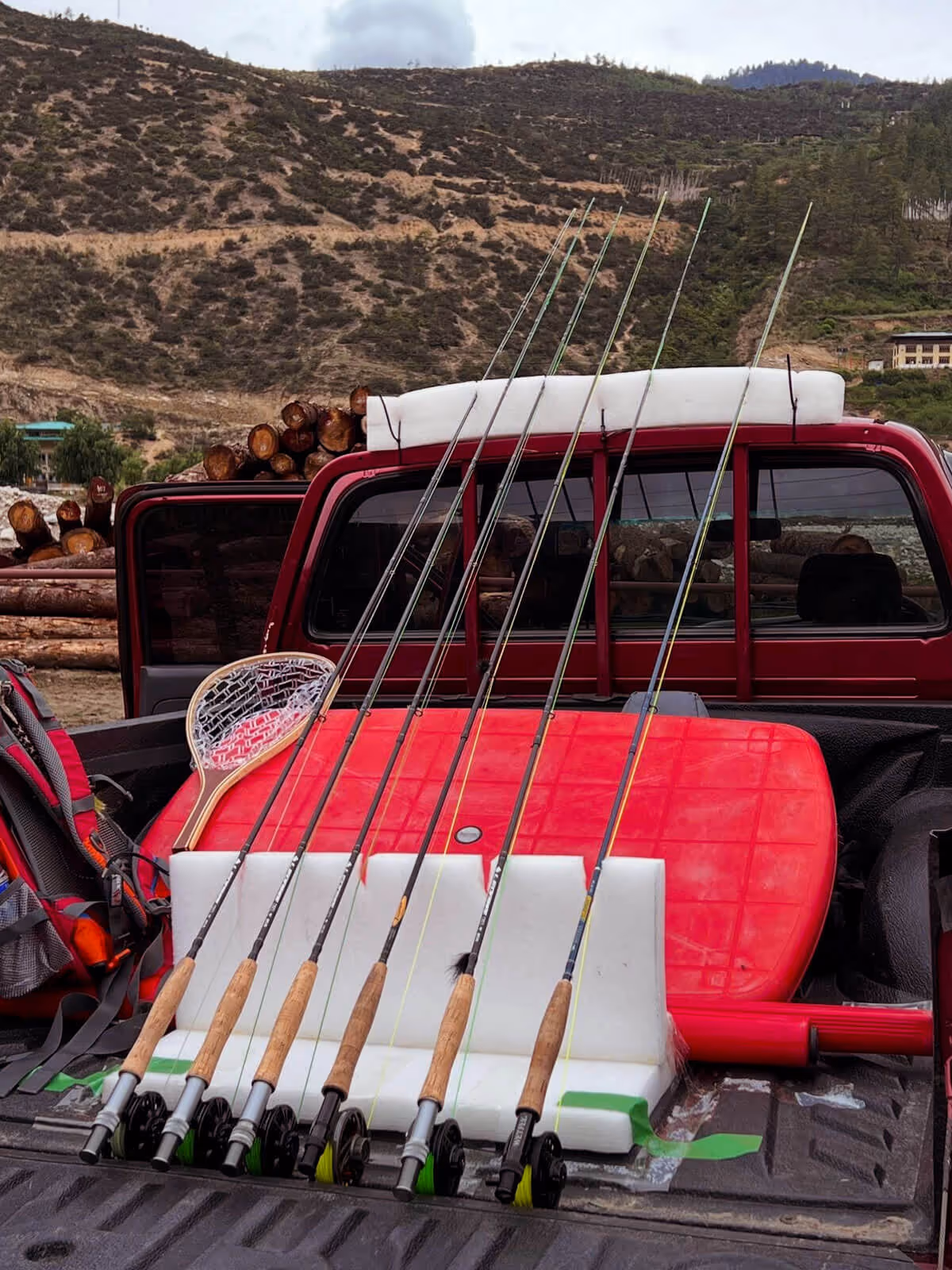 Multiple fishing rods and a net neatly arranged in the back of a red pickup truck, ready for an angling adventure in Bhutan’s rugged terrain.