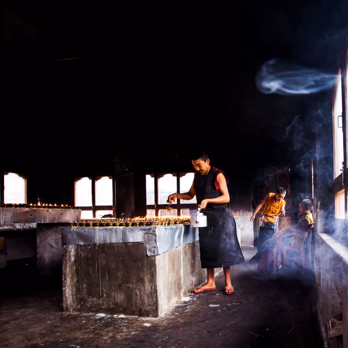 Monk preparing butter lamps in a dimly lit temple