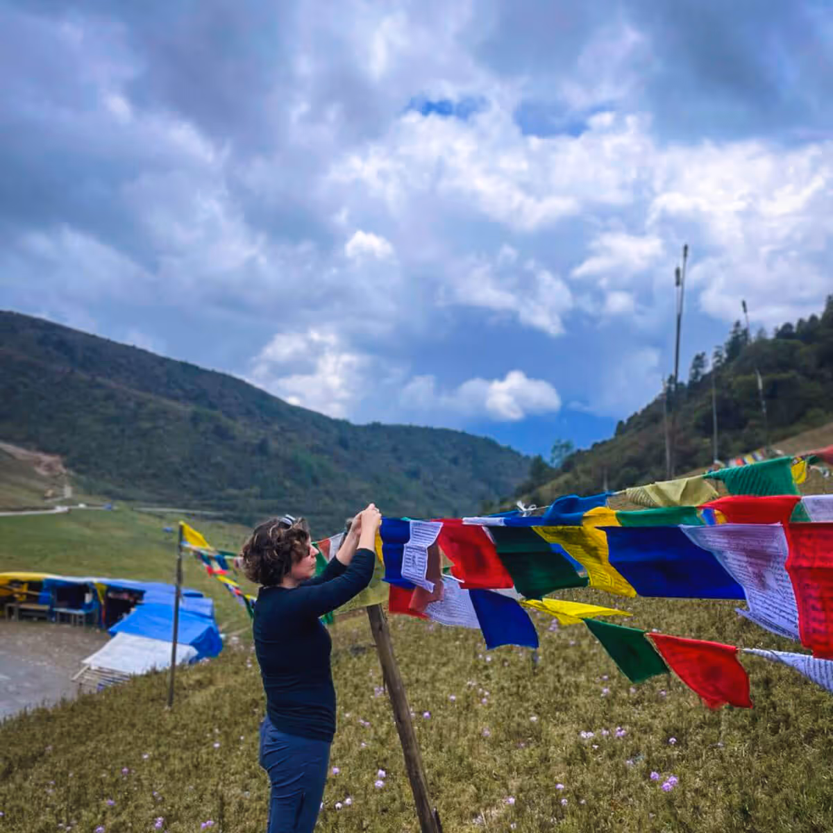 Traveler tying colorful prayer flags in a mountain meadow in Bhutan.