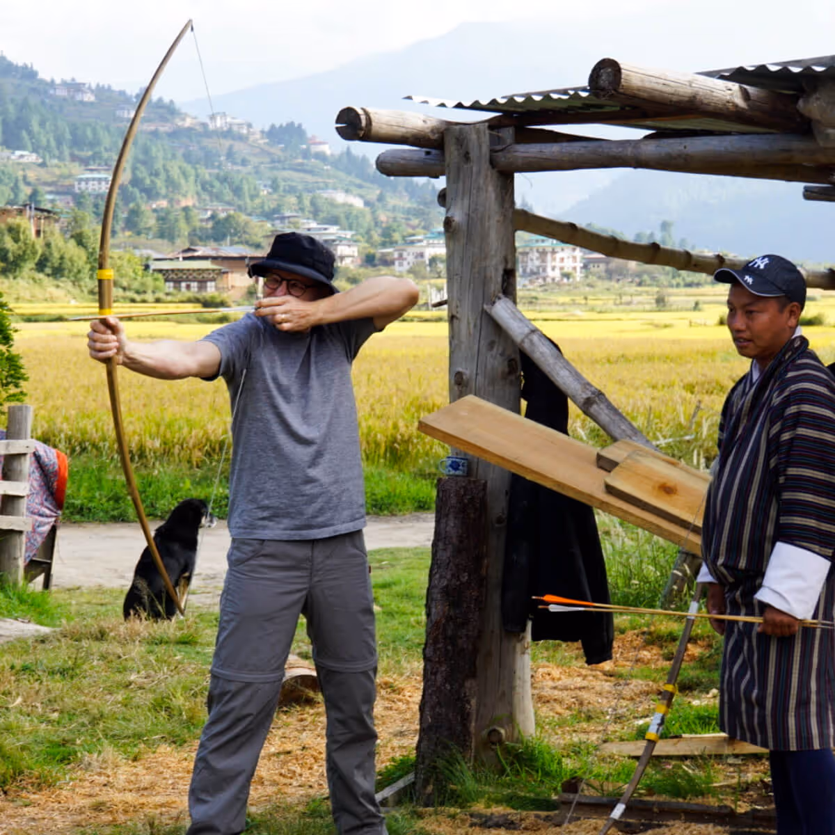 Traveler practicing traditional archery in a Bhutanese village with local guidance.
