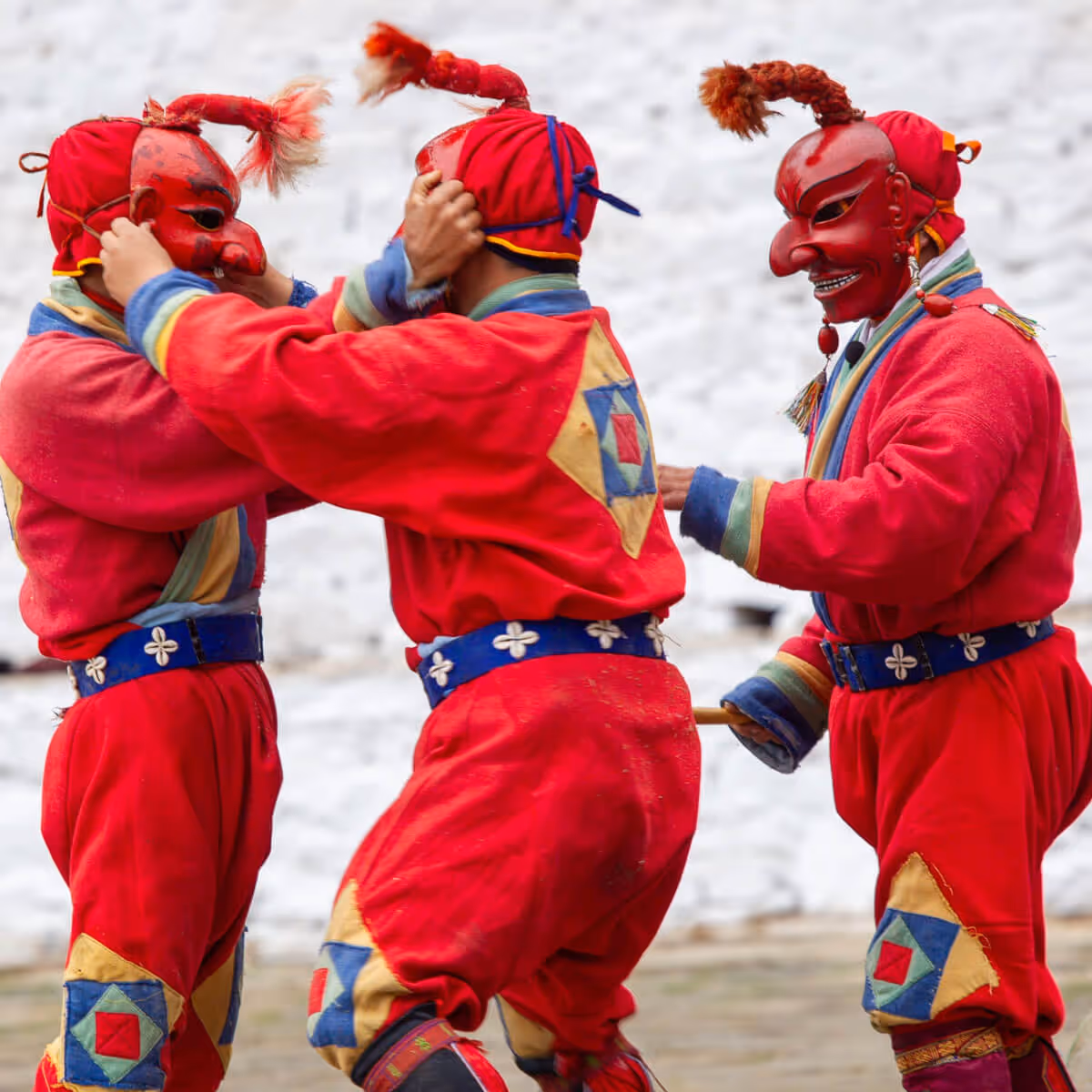 Festival clowns (atsaras) in red costumes playfully pulling each other’s ears during a performance.